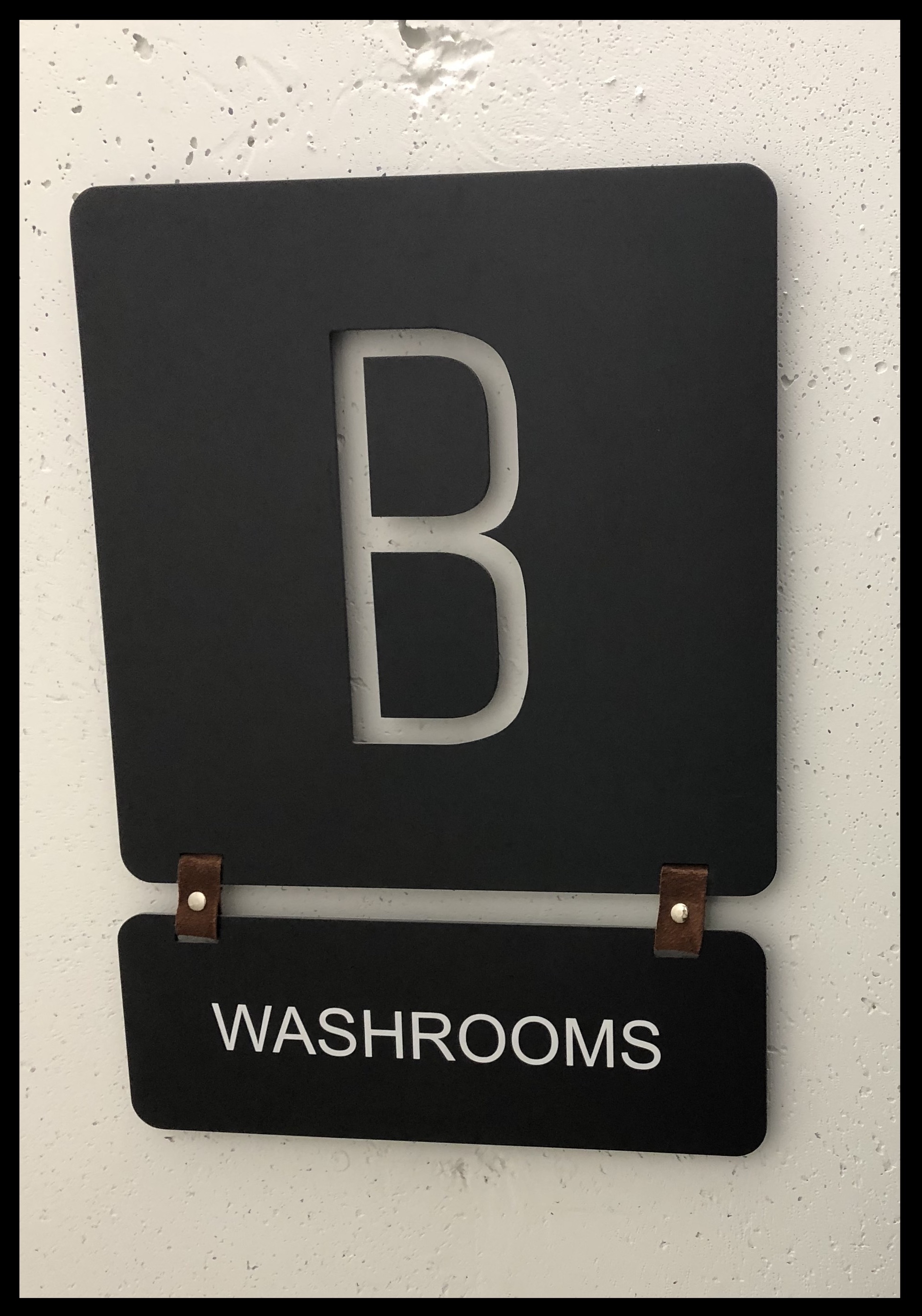 Signage that says "washrooms" hanging underneath a giant letter B with leather or suede loops. 