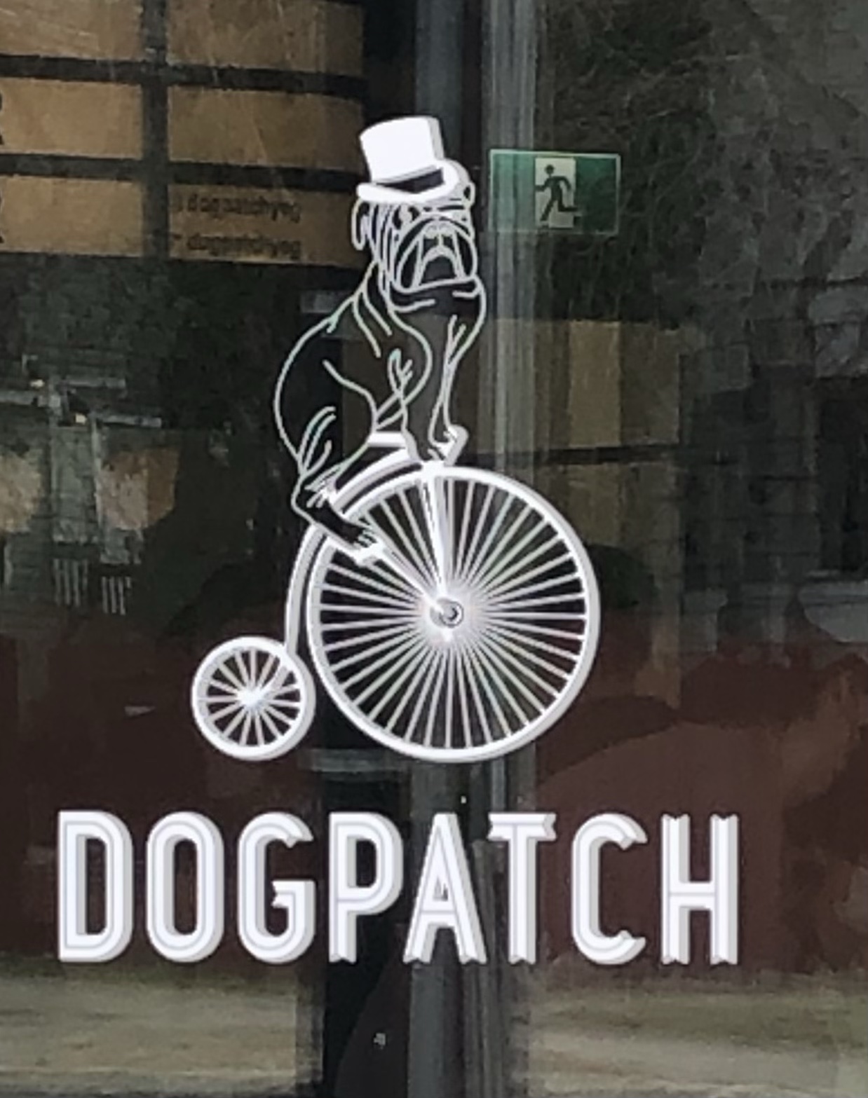 Bulldog riding a penny-farthing bicycle on the Dogpatch's glass front door.