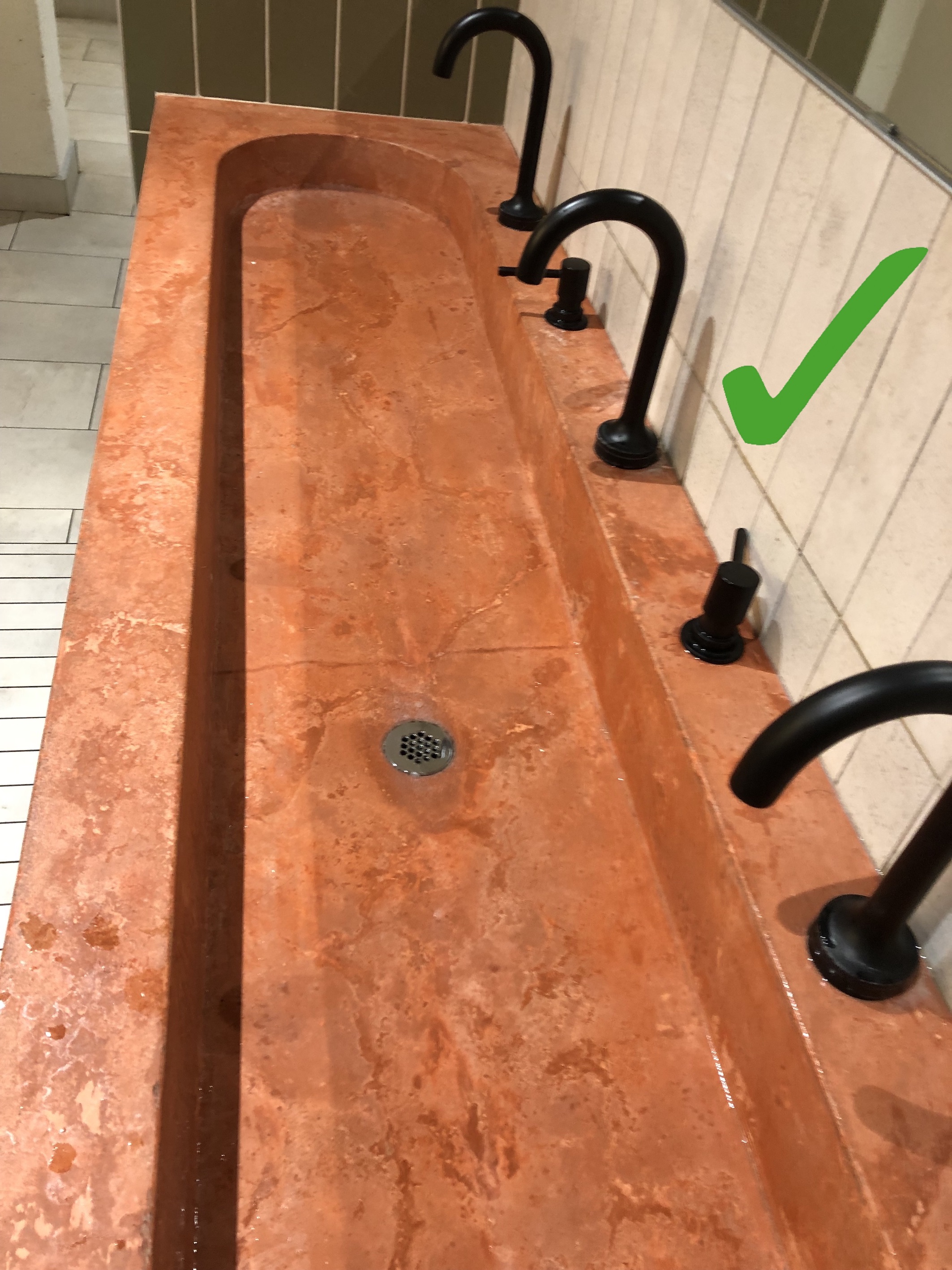 A slender brick red wash basin with black faucets and a green check mark. 