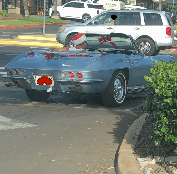 A convertible car decorated with tinsel and Christmas bows. The driver is wearing a Santa Clause hat and sunglasses.