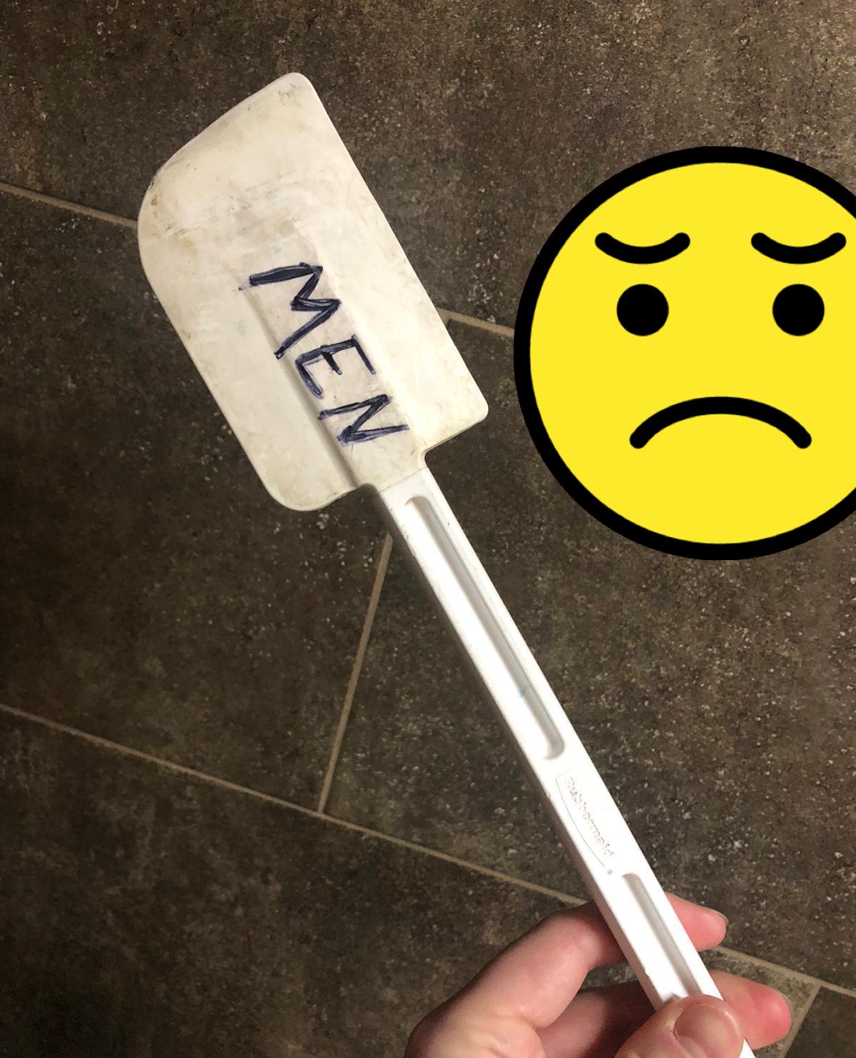 A white spreading/scraping spatula labeled "MEN" in sloppy sharpie writing. The spatula is visibly dirty with grime and crud on it. 
